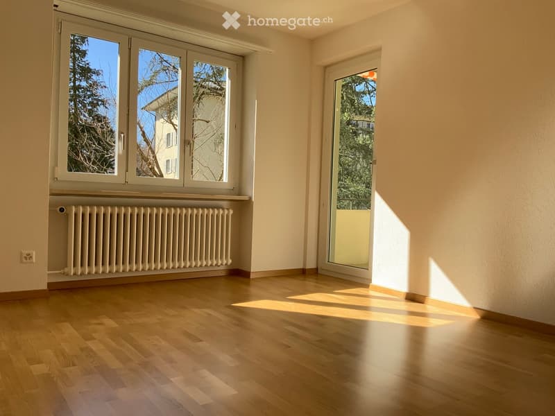 Empty room with wooden flooring, large windows, radiator, and sliding glass door leading to outdoor area.