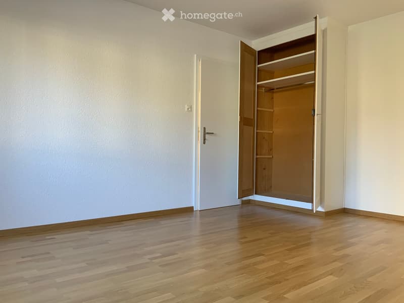Empty room with wooden flooring, white walls, and an open closet with empty shelves.