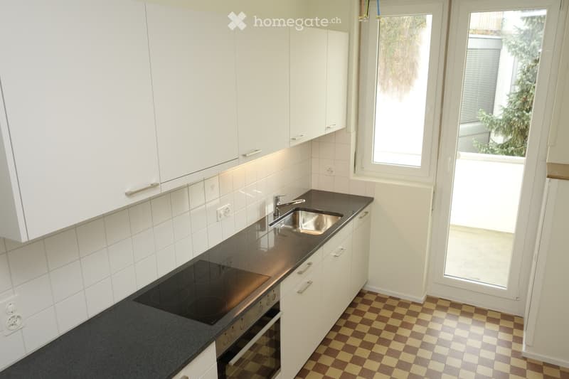 Modern kitchen with white cabinets, black countertop, electric stove, sink, and checkered floor.