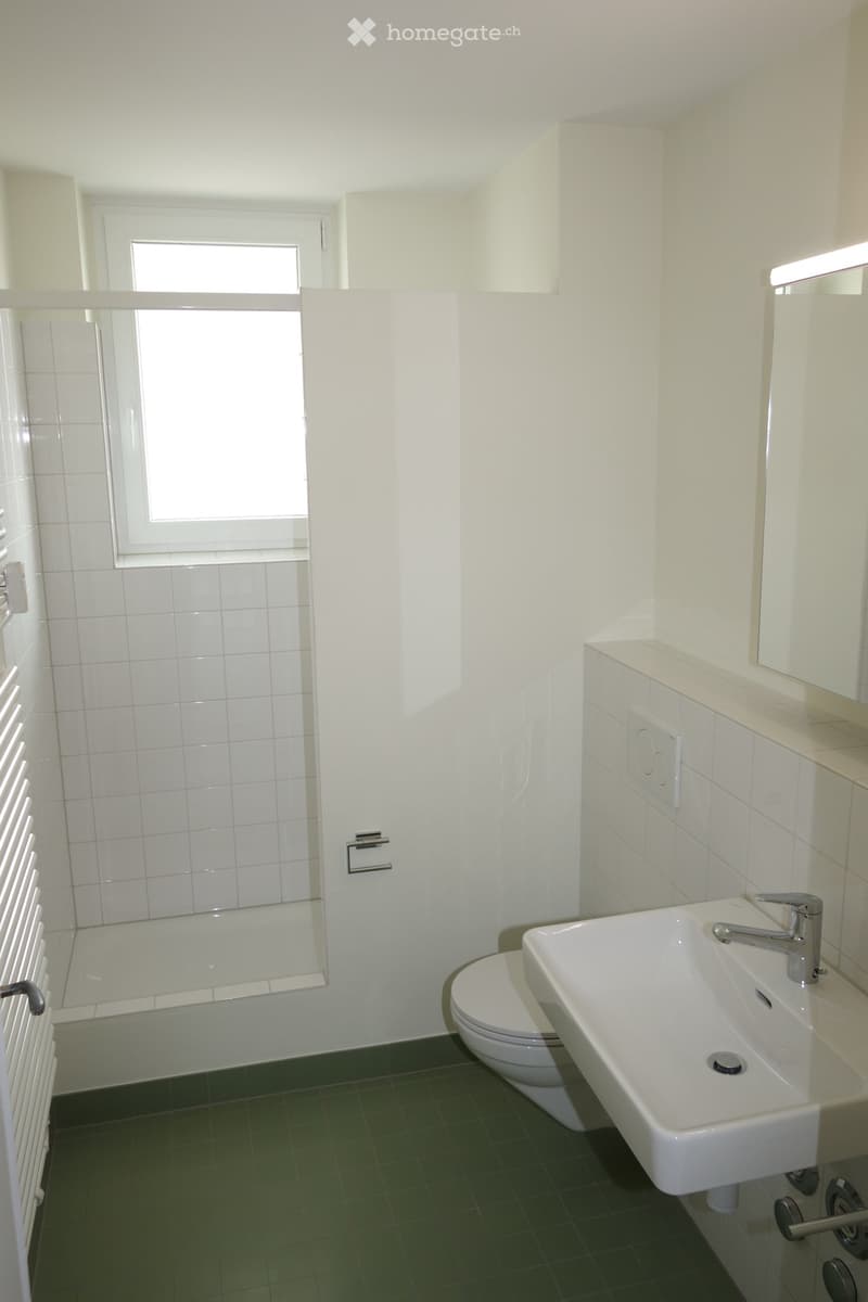 Modern bathroom with white tiles, green floor, sink, toilet, bathtub, mirror, and radiator.