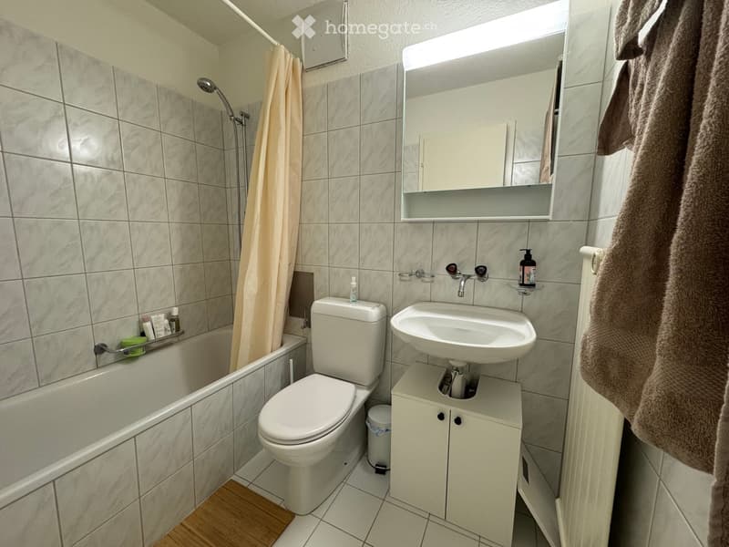 Modern bathroom with tiled walls, a bathtub, toilet, sink, mirror, and a towel hanging on the side.