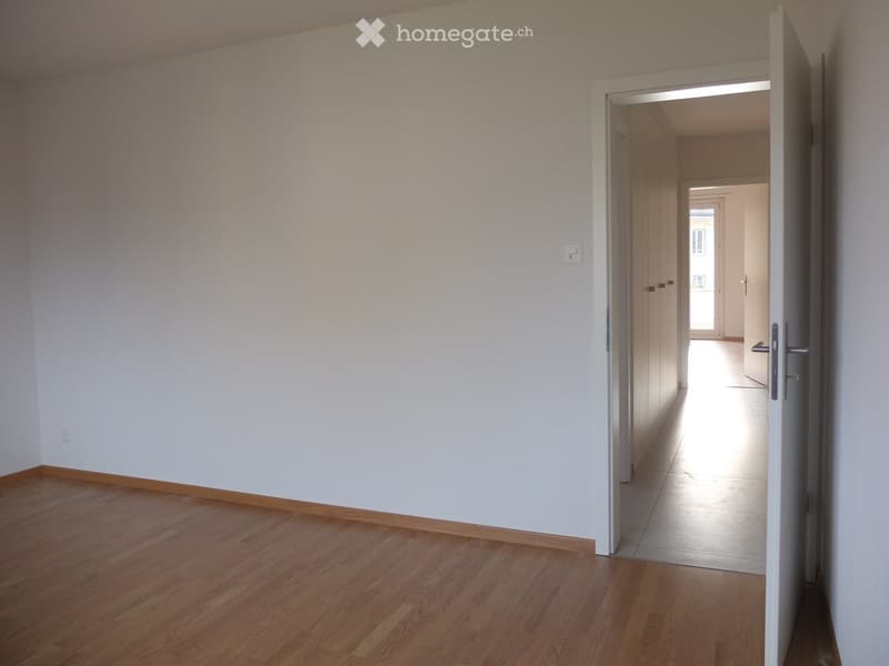 Empty room with wooden flooring and white walls, featuring an open doorway leading to another area.
