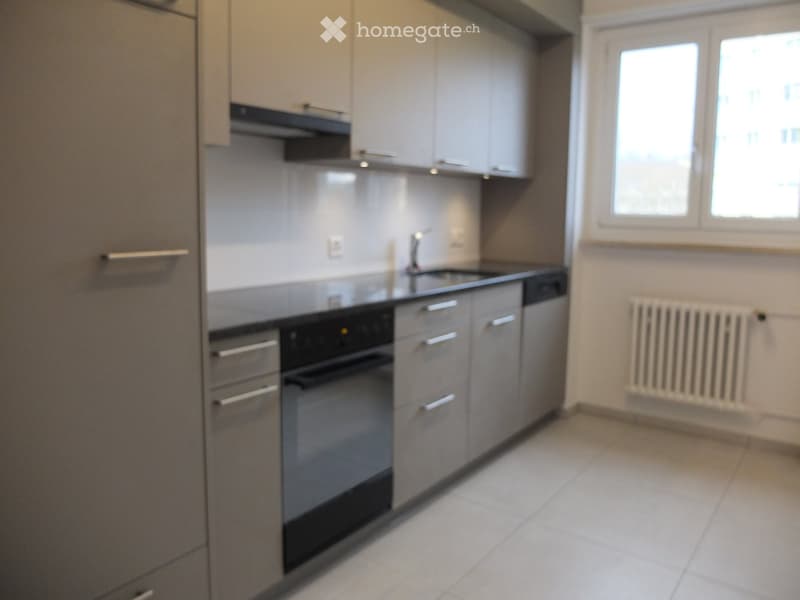 Modern kitchen with light grey cabinets, stainless steel appliances, and a white tiled floor.