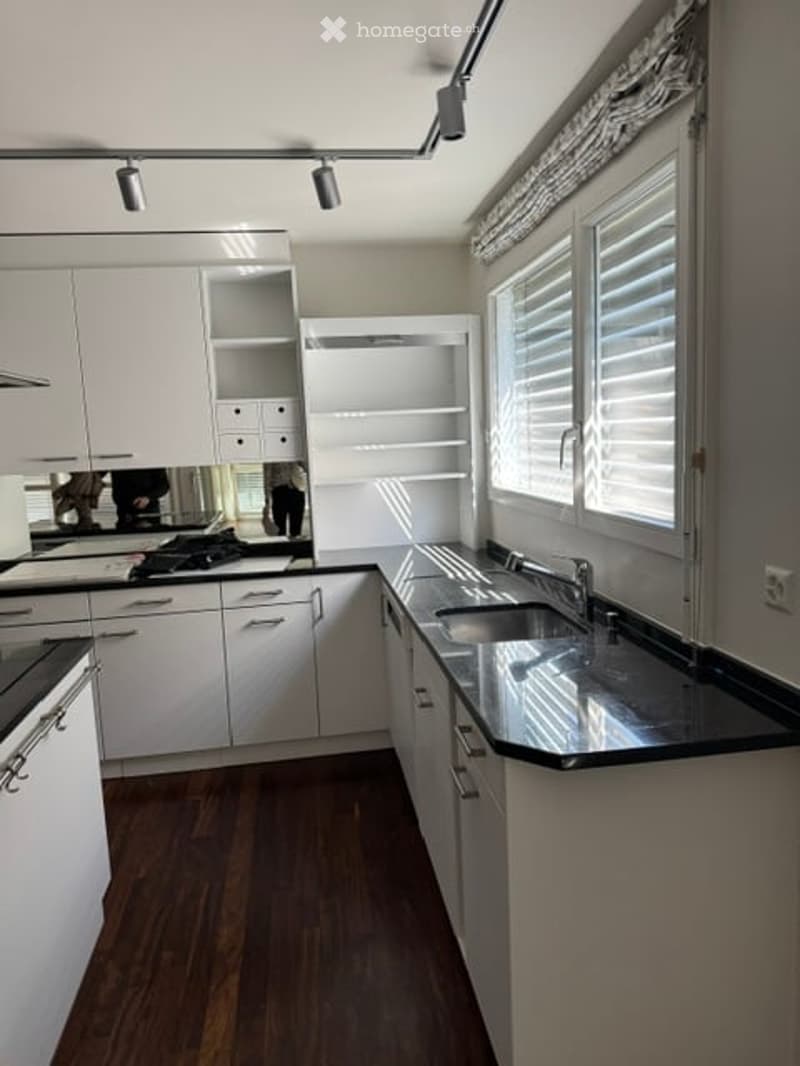 Modern kitchen with white cabinets, stainless steel appliances, and a dark countertop. Features a large window with blinds and recessed lighting.