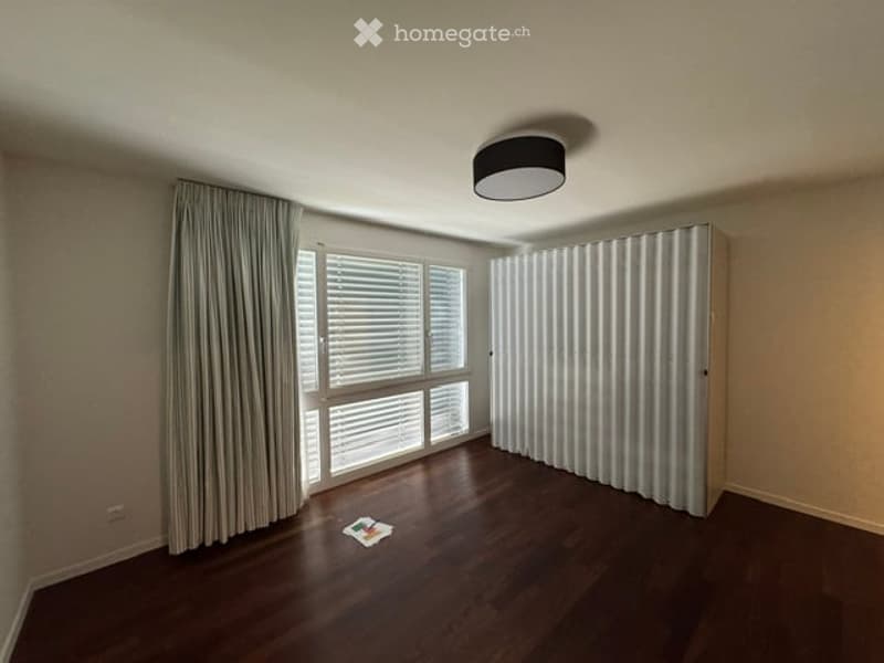 Empty room with wooden flooring, large window with blinds, and a tall white closet. No furniture or equipment present.