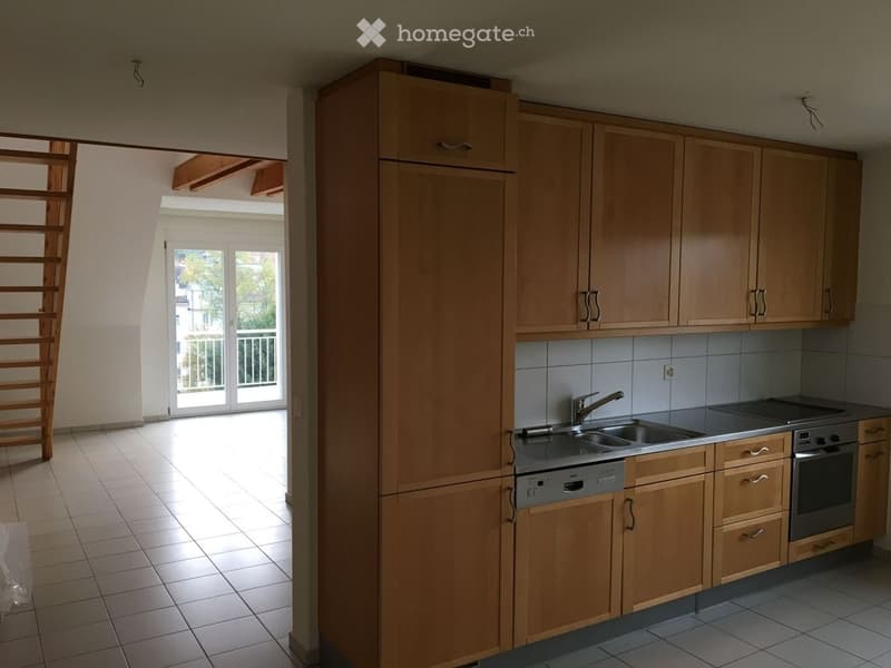 Modern kitchen with light wooden cabinets, stainless steel sink, faucet, oven, and dishwasher. The kitchen has a tiled floor and opens to a balcony area with a view of the outside.