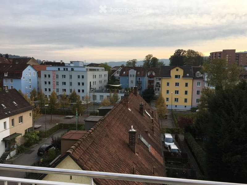 Balcony overlooking a residential area with multiple buildings, trees, and parked cars.