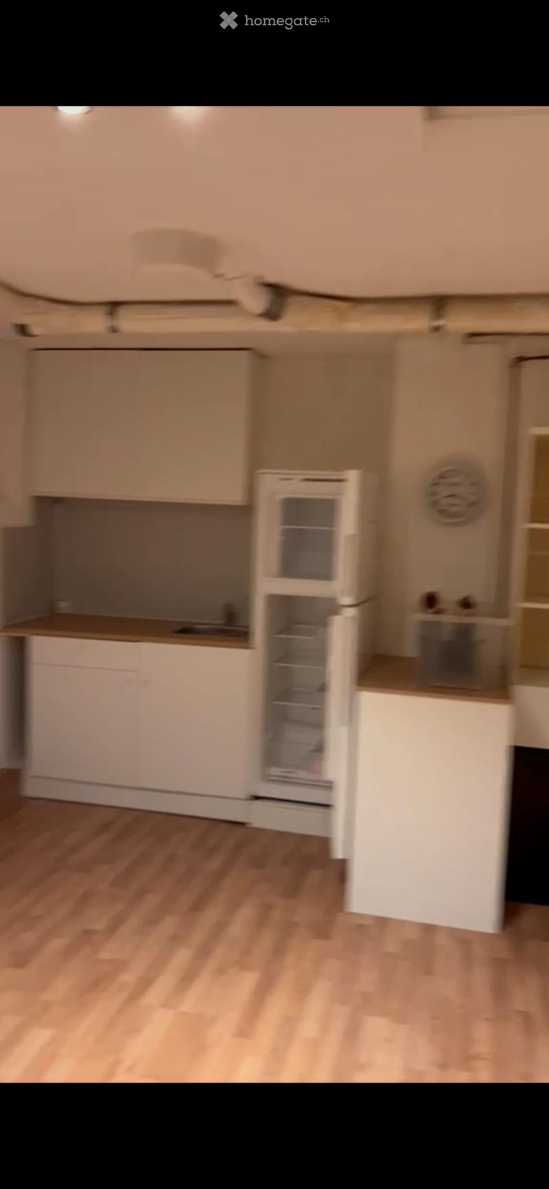 Modern kitchen with light-colored cabinets, a refrigerator, and wooden flooring.