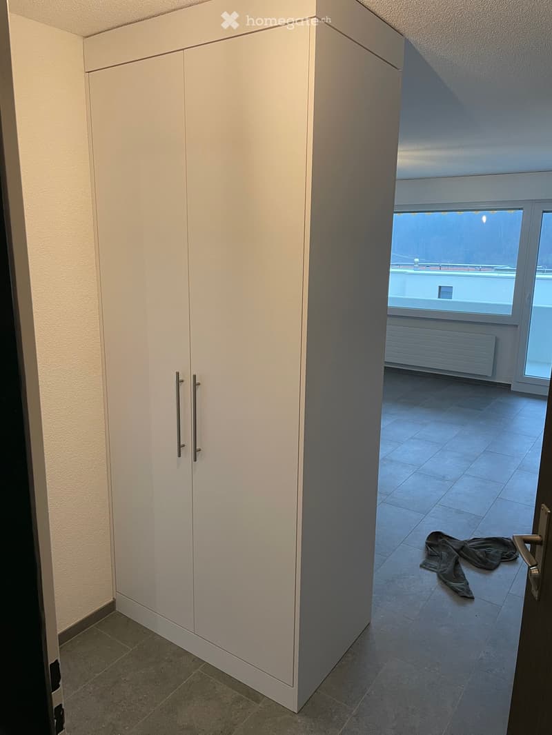 Empty room with tiled floor, white built-in wardrobe, and a view of a balcony area through an open doorway.