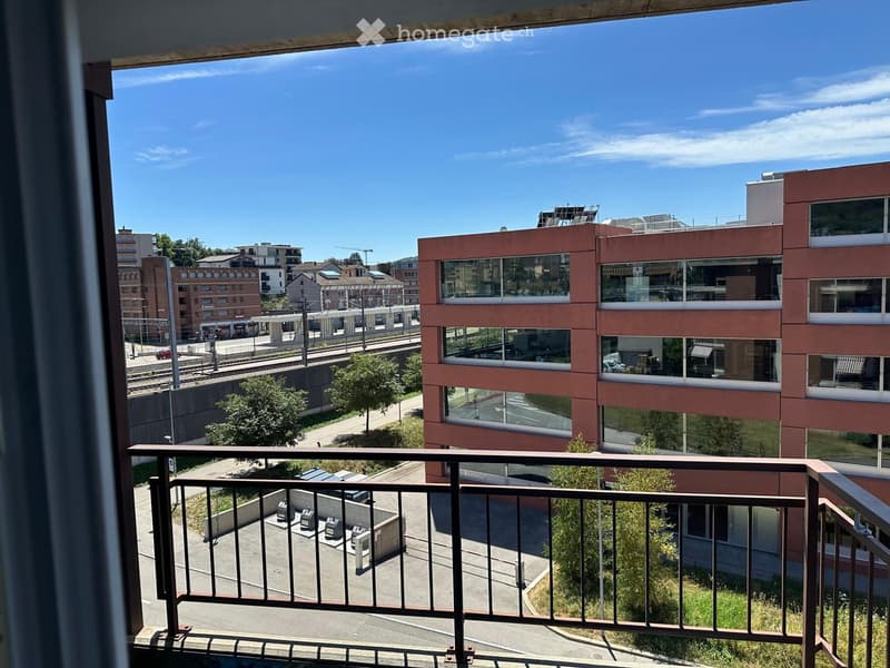 Balcony overlooking a cityscape with modern buildings, a train track, and some greenery.
