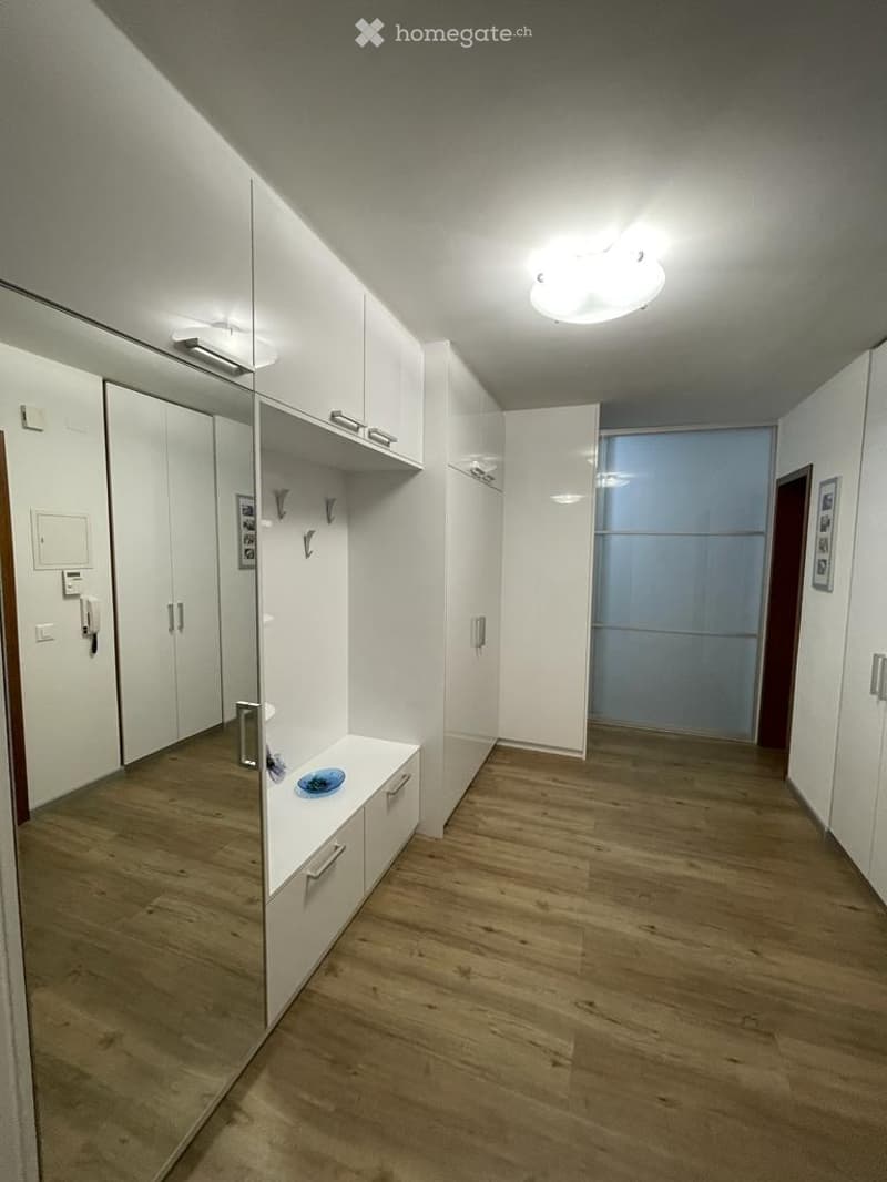 Modern hallway with white built-in wardrobes, wooden flooring, and a small bench with a decorative bowl.