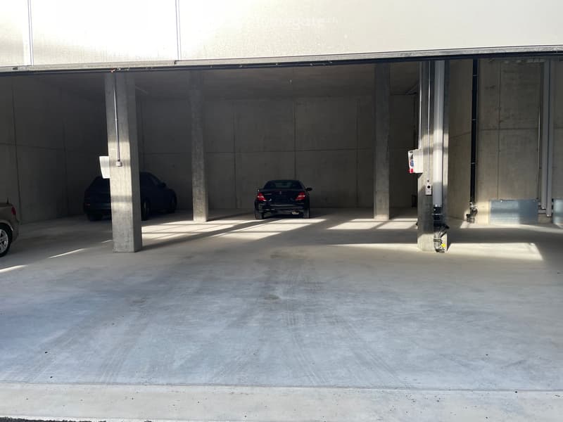 Underground parking area with concrete pillars and several parked cars.