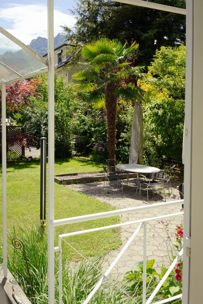 Garden with a table and chairs, surrounded by lush greenery and a view of mountains.