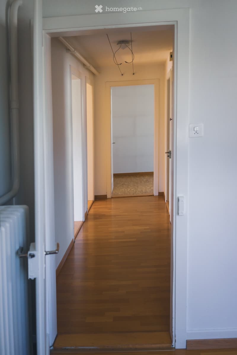 Empty hallway with wooden flooring, white walls, and multiple doors leading to other rooms.