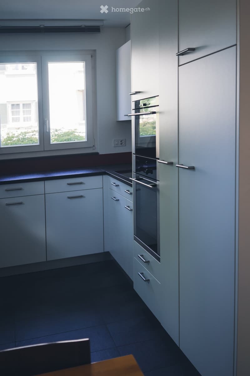 Modern kitchen with white cabinets, stainless steel oven, dark countertops, and tiled floor.