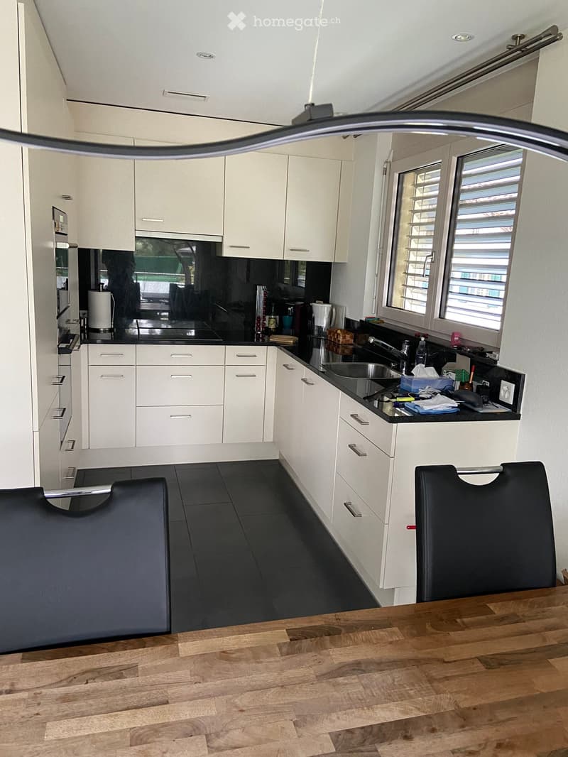 Modern kitchen with white cabinets, black countertops, and stainless steel appliances. Features a wooden dining table with two black stools.