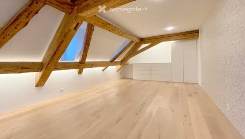 Empty attic space with exposed wooden beams, skylights, and light wooden flooring.