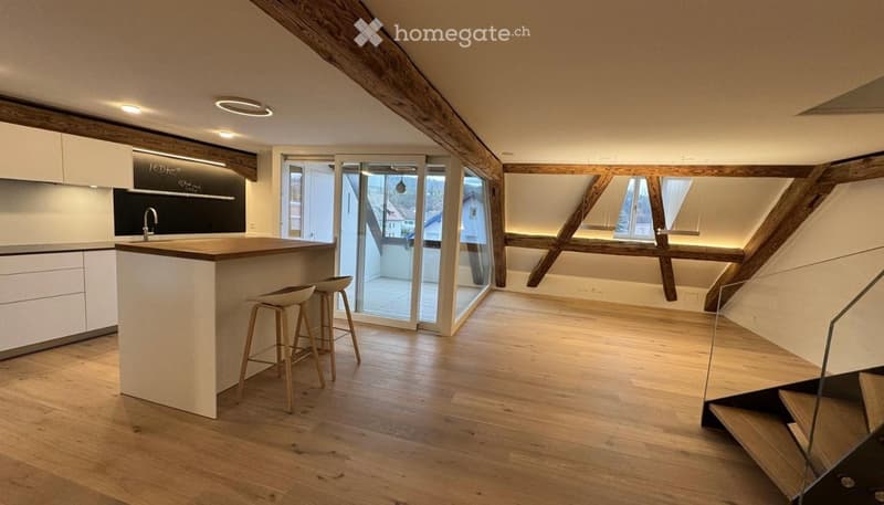Modern kitchen with wooden beams, white cabinets, a central island, and bar stools. Large windows and a glass door lead to a balcony.