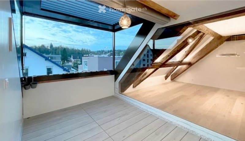 Modern balcony with large glass windows, wooden slatted floor, and a hanging light fixture.