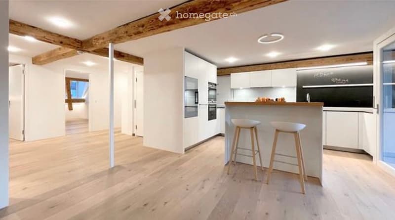Modern kitchen with white cabinets, wooden bar counter, two stools, and built-in appliances including an oven and refrigerator.