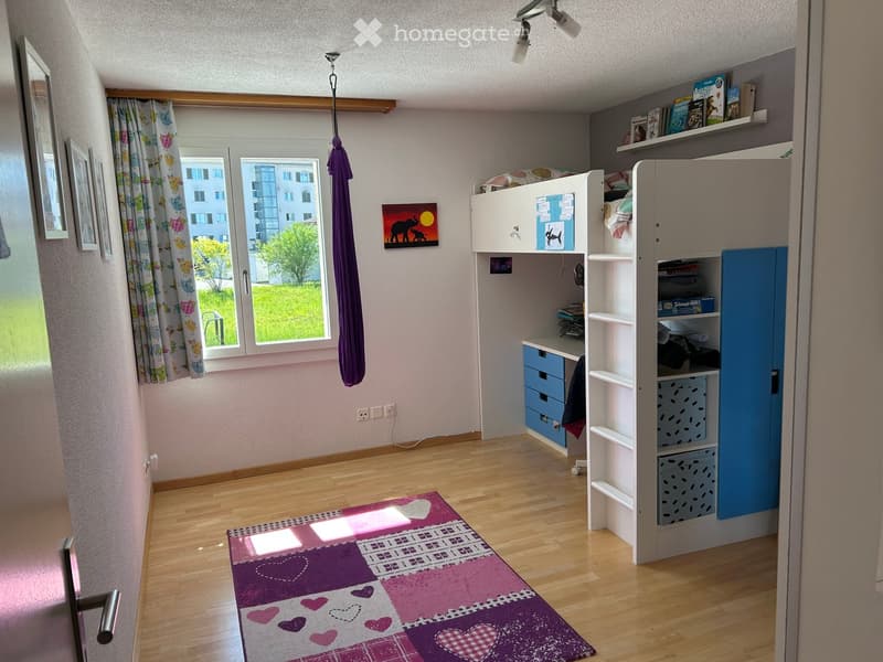 Cozy bedroom with wooden flooring, bunk bed, desk, bookshelf, and colorful rug.
