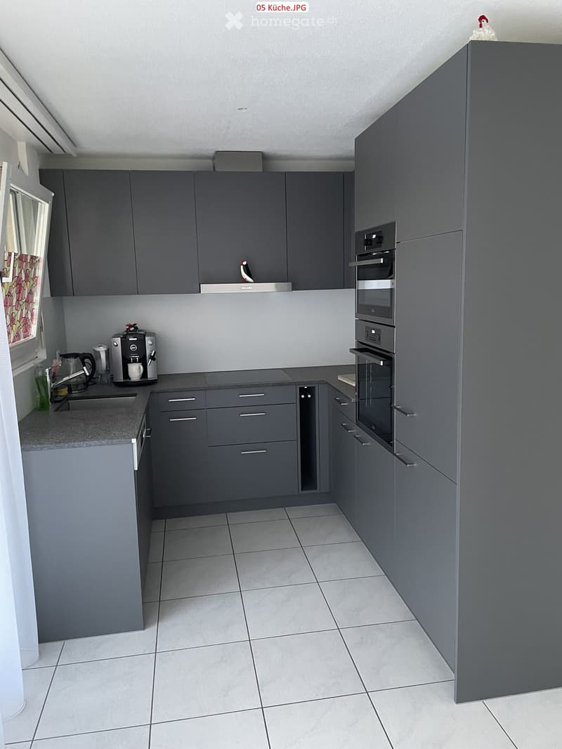 Modern kitchen with grey cabinets, tiled floor, and stainless steel appliances including a coffee maker, oven, and sink.