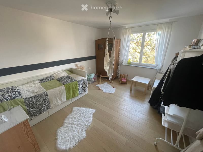 Cozy bedroom with wooden flooring, a bed with a patchwork quilt, a small table, a chair, a wardrobe, and a fluffy rug.