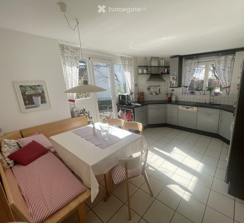 Bright living and dining area with a sofa, dining table, chairs, and a modern kitchen with cabinets, appliances, and a sink.