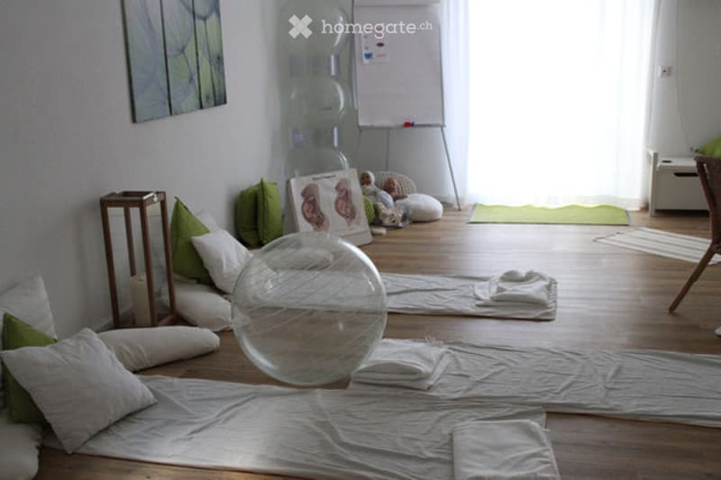 A yoga or meditation room with wooden flooring, several pillows, a large transparent balloon, a small table, and a picture frame on the wall.