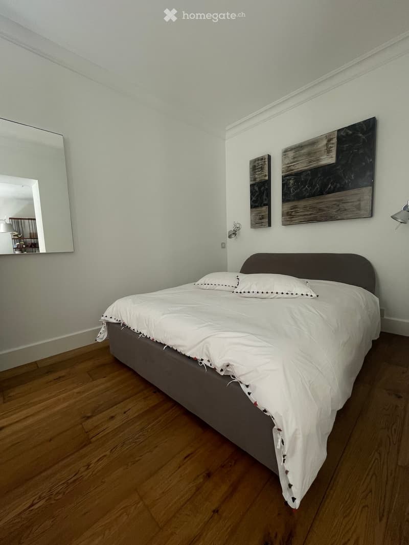Modern bedroom with a neatly made bed, white bedding, wooden flooring, and two pieces of wall art.