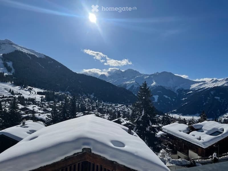 Wide view of a snowy mountain with small buildings in the foreground.