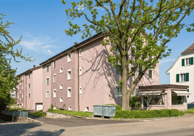 A multi-story residential building with pink siding, multiple windows, and a small storefront at the ground level.