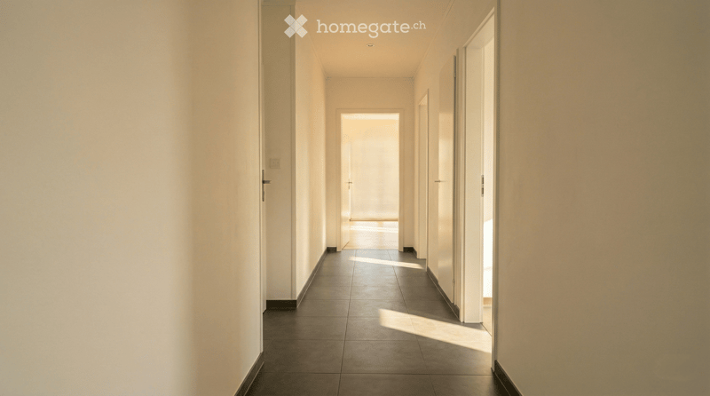 Empty hallway with white walls, dark tiled floor, and several doors leading to other rooms.