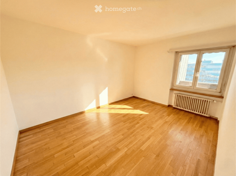 Empty room with wooden flooring and white walls, featuring a large window with a radiator below it.