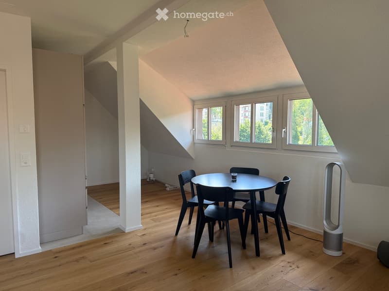Bright, modern room with wooden flooring, large windows, a round dining table with four chairs, and an air purifier in the corner.