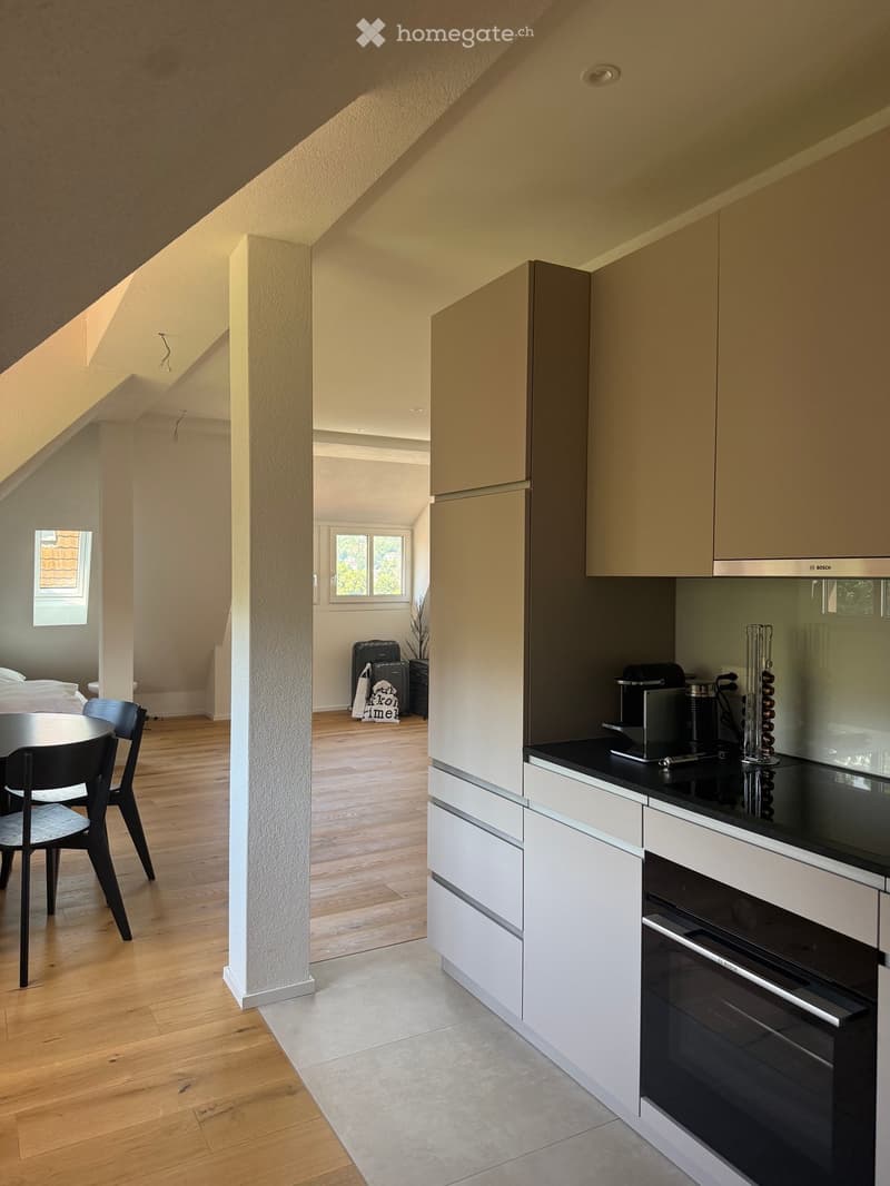 Modern kitchen with white cabinets, black countertops, and stainless steel appliances. Adjacent dining area with wooden flooring and black chairs around a round table.