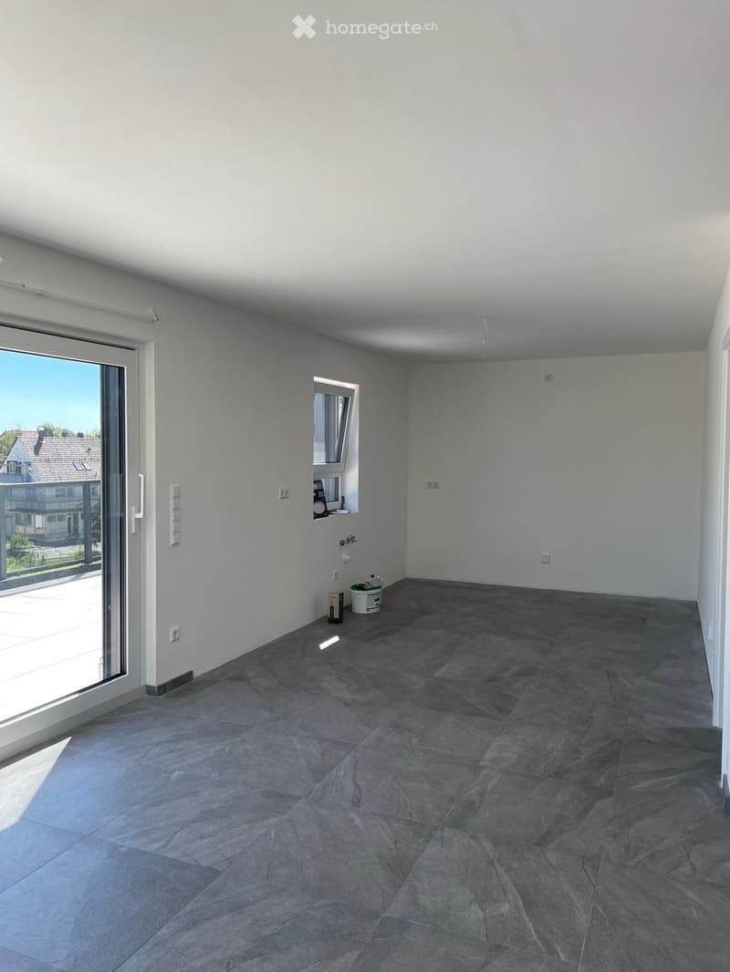 Empty room with grey tiled floor, white walls, large sliding glass door, and small window. No furniture or equipment present.