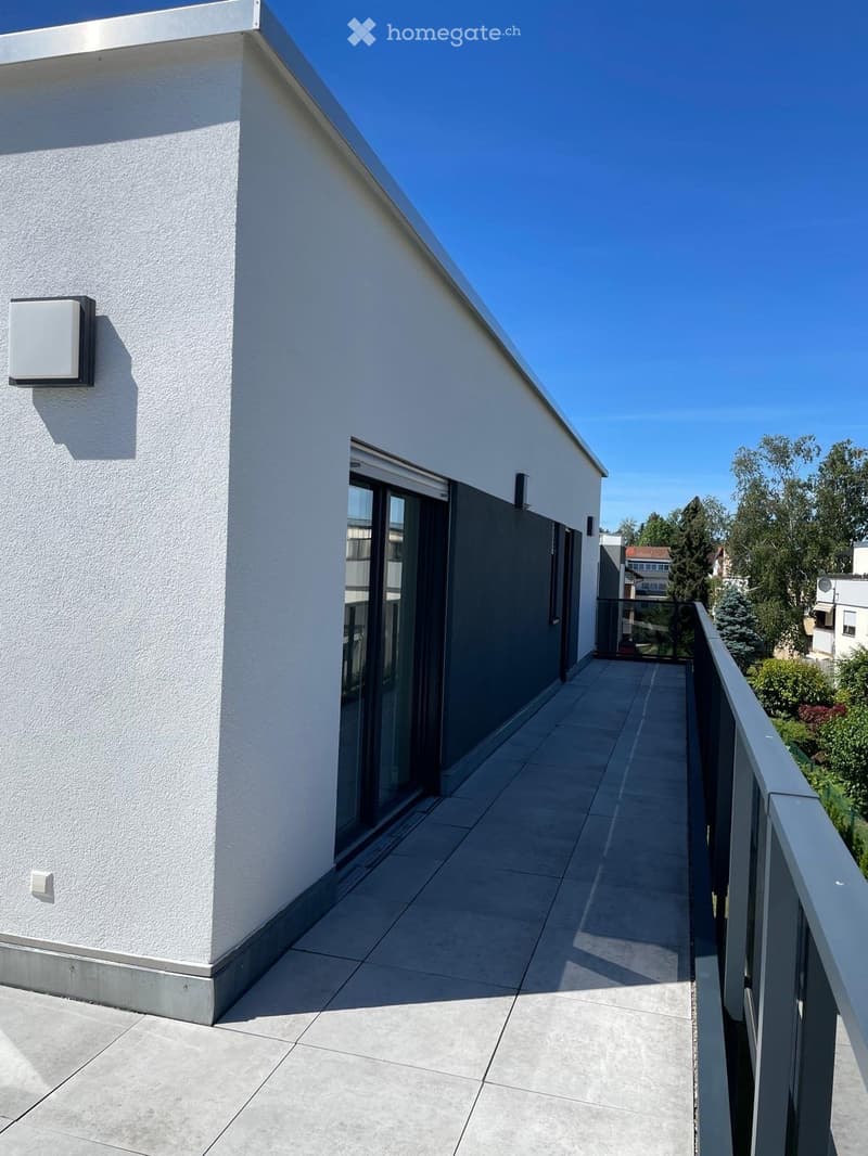 Modern balcony with tiled floor, glass railing, and sliding glass door leading to the interior.