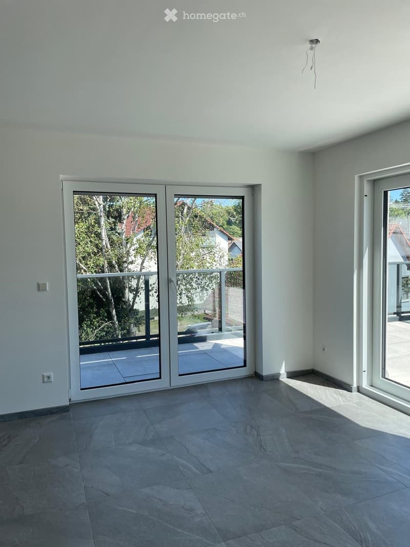 Empty room with light grey tiled floor, white walls, and large sliding glass doors leading to a balcony or outdoor area.