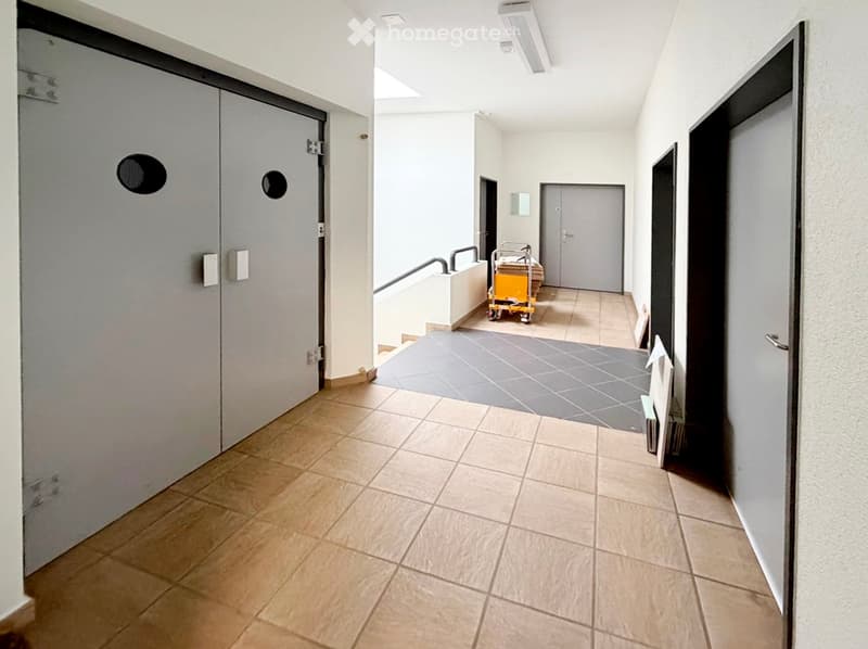 Clean, modern hallway with tiled flooring, white walls, and several doors. A small cart is visible in the background.