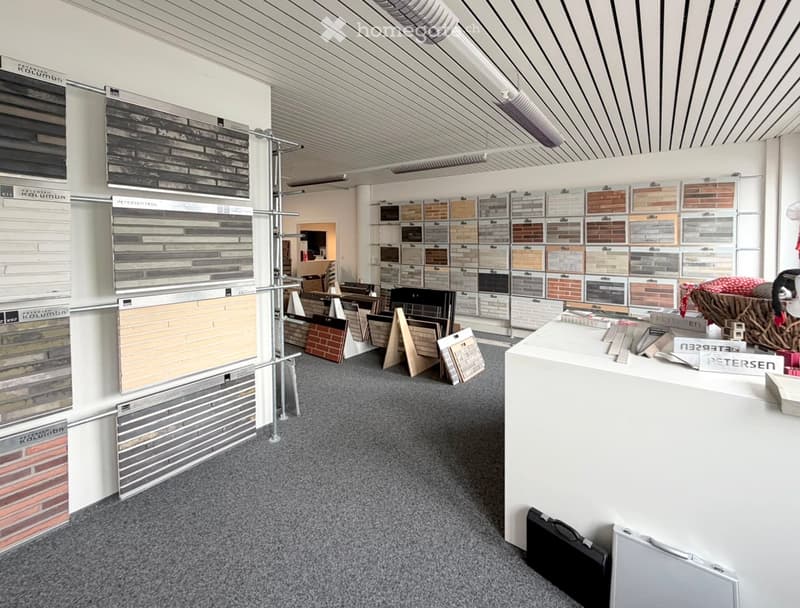 Interior of a tile and material showroom with a reception desk, sample displays, and various tile samples arranged on walls and tables.