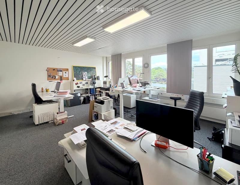 Office space with desks, chairs, laptops, printers, and a large window with a view.
