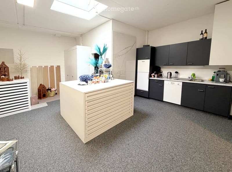 Modern kitchen with grey cabinets, white countertops, and various appliances including a refrigerator, dishwasher, coffee maker, and sink. There is a central island with a white countertop and decorative items on it.
