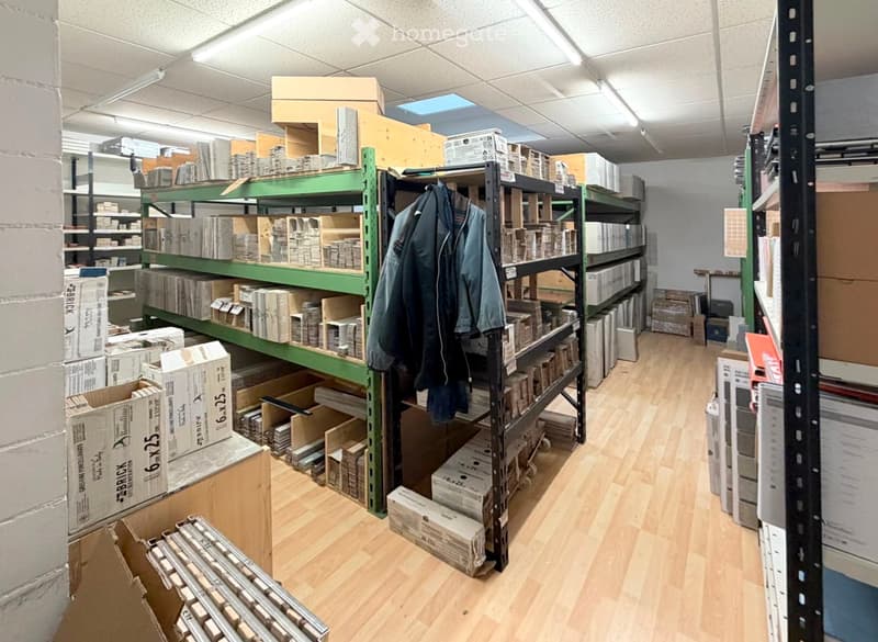 A storage room with wooden flooring, metal shelving units filled with boxes and materials, and jackets hanging on a rack.