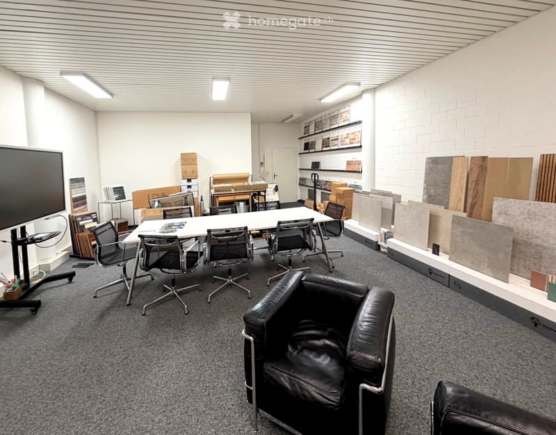Office space with a large conference table, chairs, a leather sofa, and display shelves with materials.