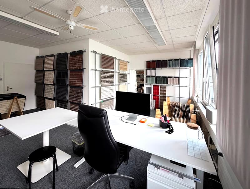 Office space with a white desk, black office chair, computer monitor, and various samples displayed on walls and shelves.