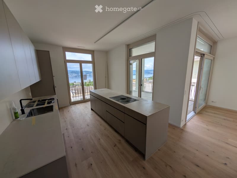 Modern kitchen with wooden flooring, white cabinets, and large windows offering a scenic view.