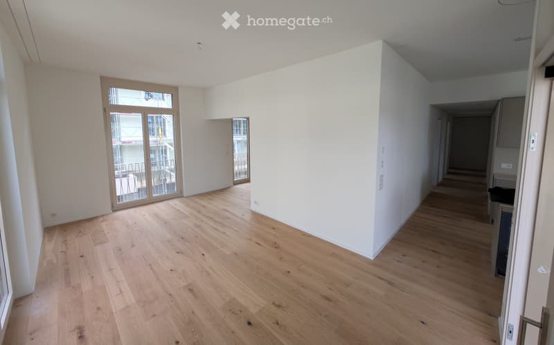 Empty room with light wooden flooring, white walls, and large glass doors leading to a balcony area.