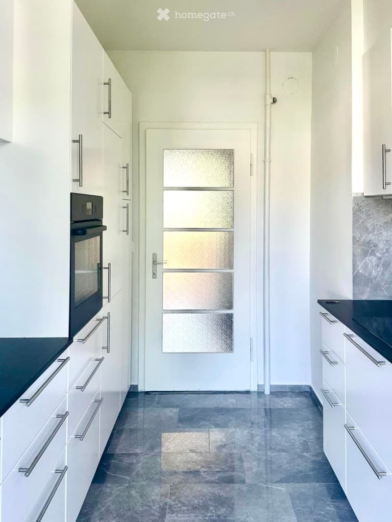 Modern hallway with white cabinets, a central door with frosted glass panels, and a tiled floor.