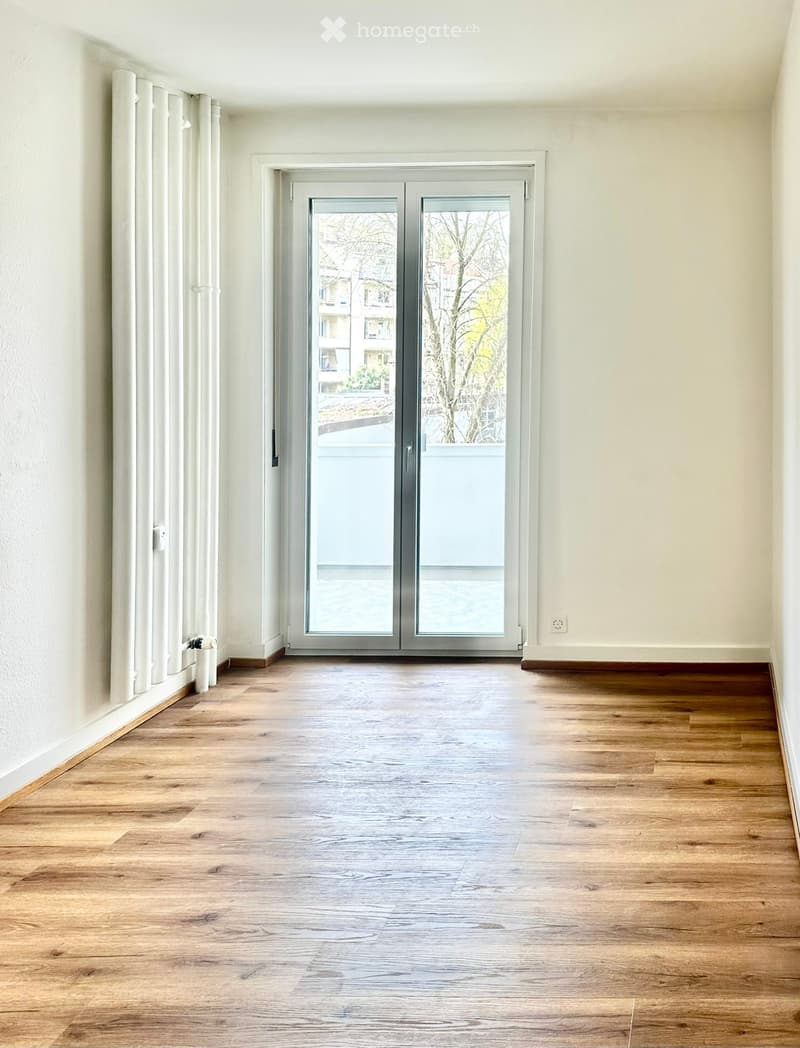 Empty room with wooden flooring, white walls, and a large sliding glass door leading to a balcony.
